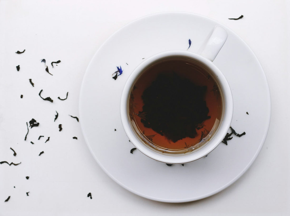 Overhead view of a white cup of black tea with loose tea leaves on a white background