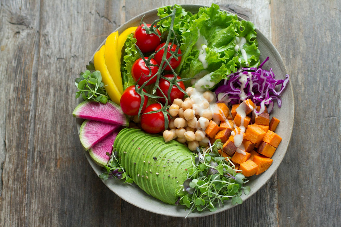 Colourful DASH-style bowl of tomatoes, avocado, chickpeas, sweet potato, red cabbage and leafy greens on a wooden table