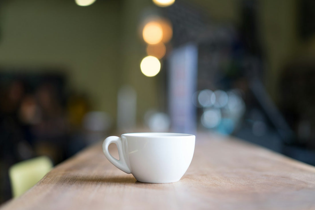 White cup of coffee on a wooden table with soft cafe lights behind it