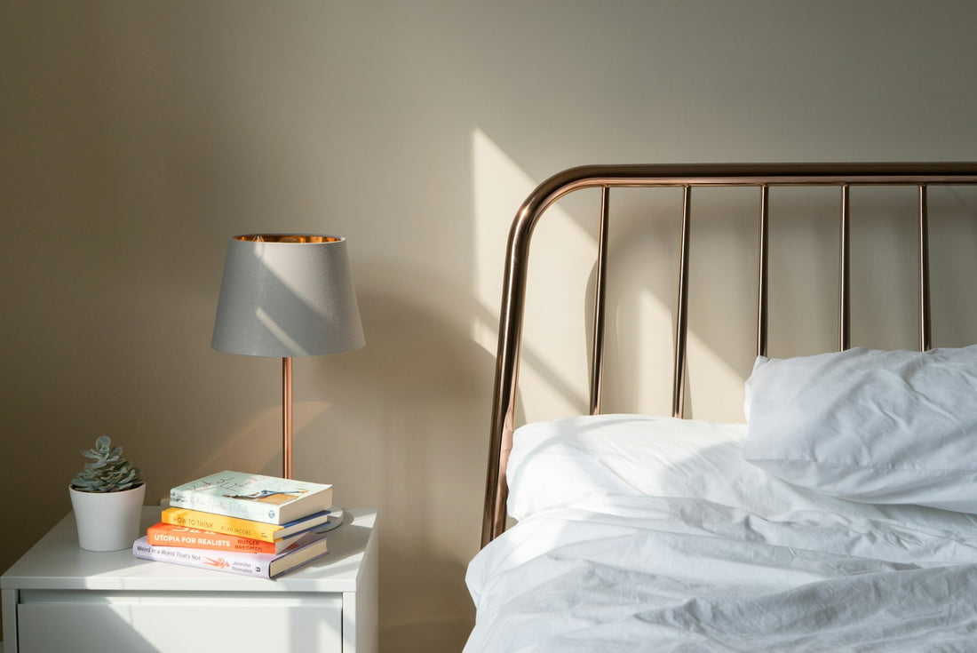 A lit bedside lamp on a nightstand beside a bed with white bedding