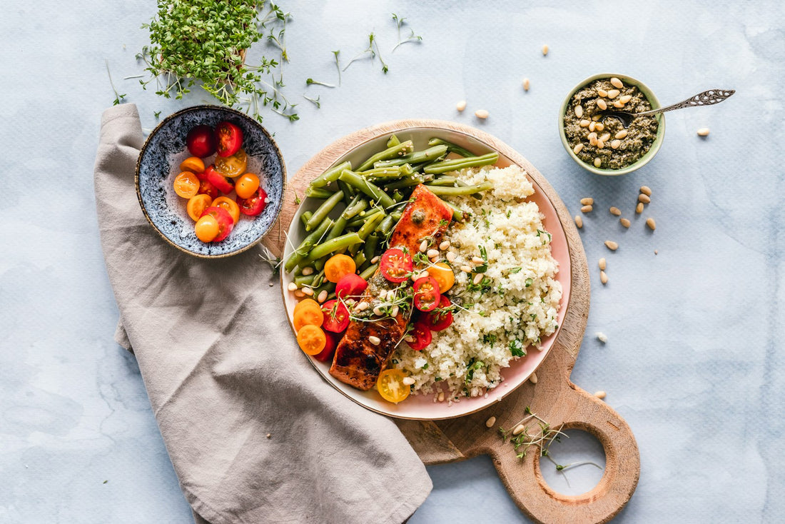 A bright plated meal of salmon with grains, green beans and tomatoes on a light table