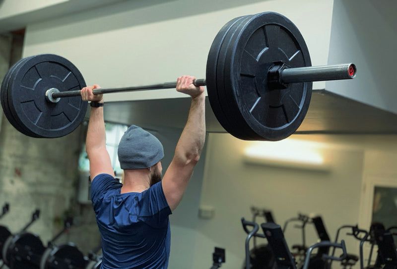 A person pressing a barbell overhead to full lockout in a bright gym