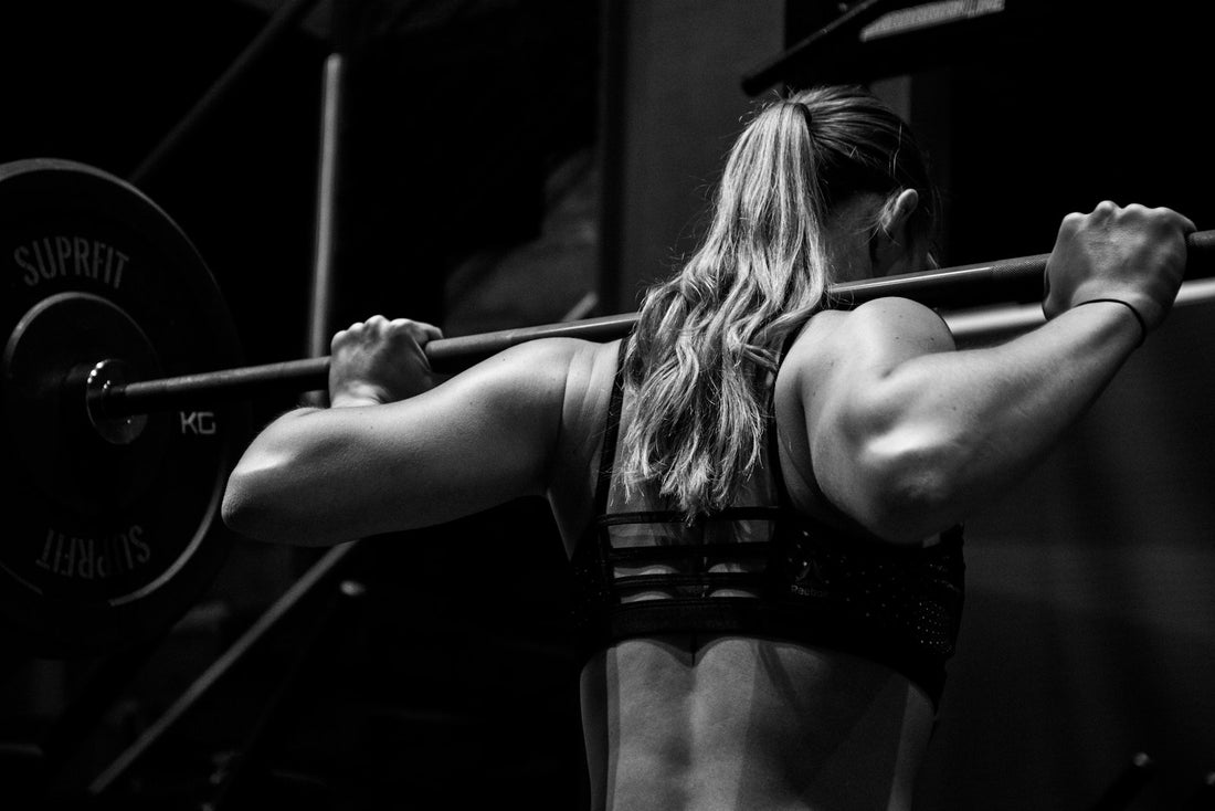 Athlete performing a barbell back squat with defined back muscles, black and white