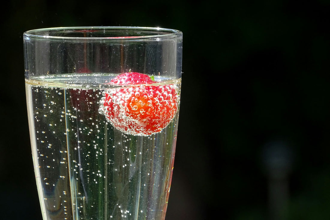 A strawberry in a tall glass of sparkling water, bubbles clinging to the fruit