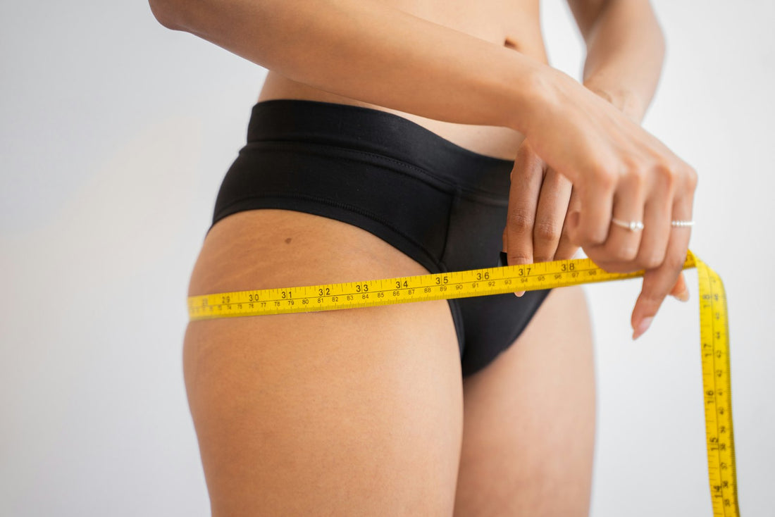 A person measuring their waist with a yellow tape measure against a white background