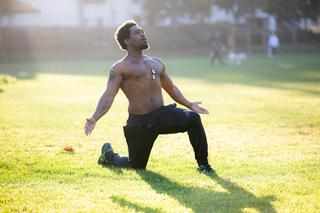 Athlete kneeling in a warm-up stretch on sunlit green grass outdoors