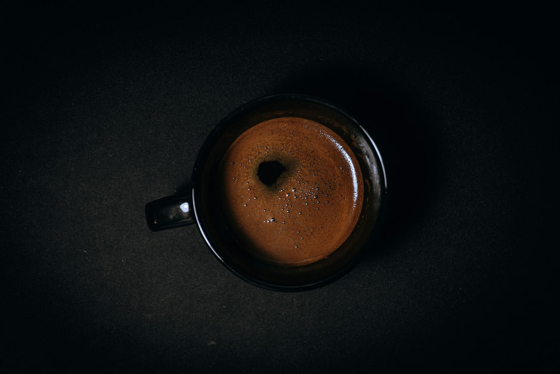 A black ceramic mug of freshly brewed coffee on a dark surface
