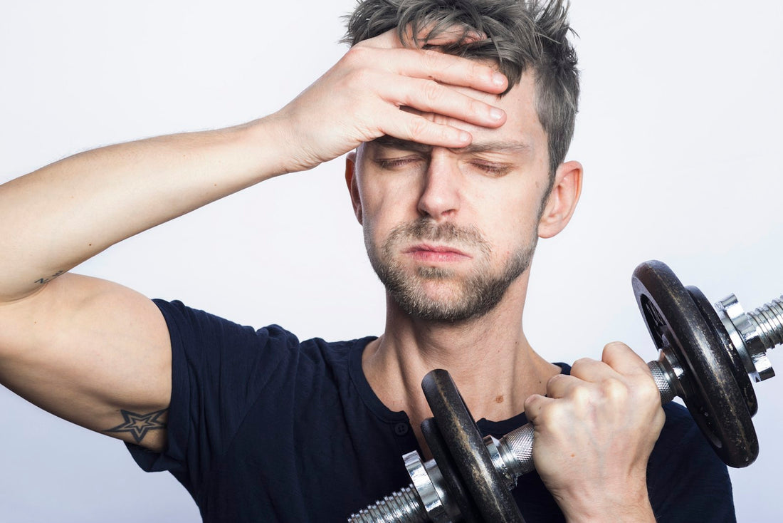 Man wiping his forehead while holding a dumbbell during a workout
