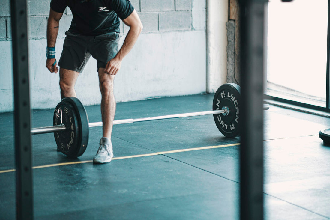A person standing over a loaded barbell in a bright gym, resting between sets