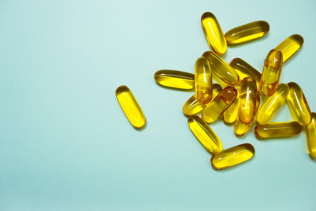 Bright yellow gel supplement capsules scattered on a pale blue background