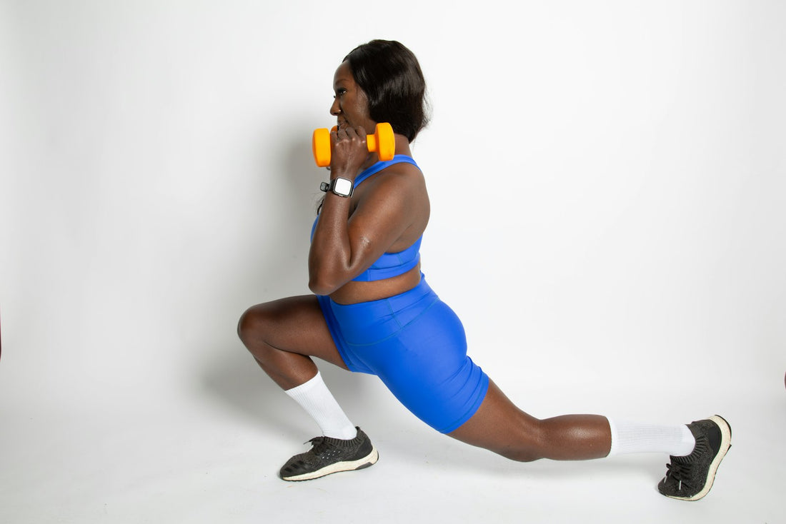 A woman doing a lunge with dumbbells in a bright studio