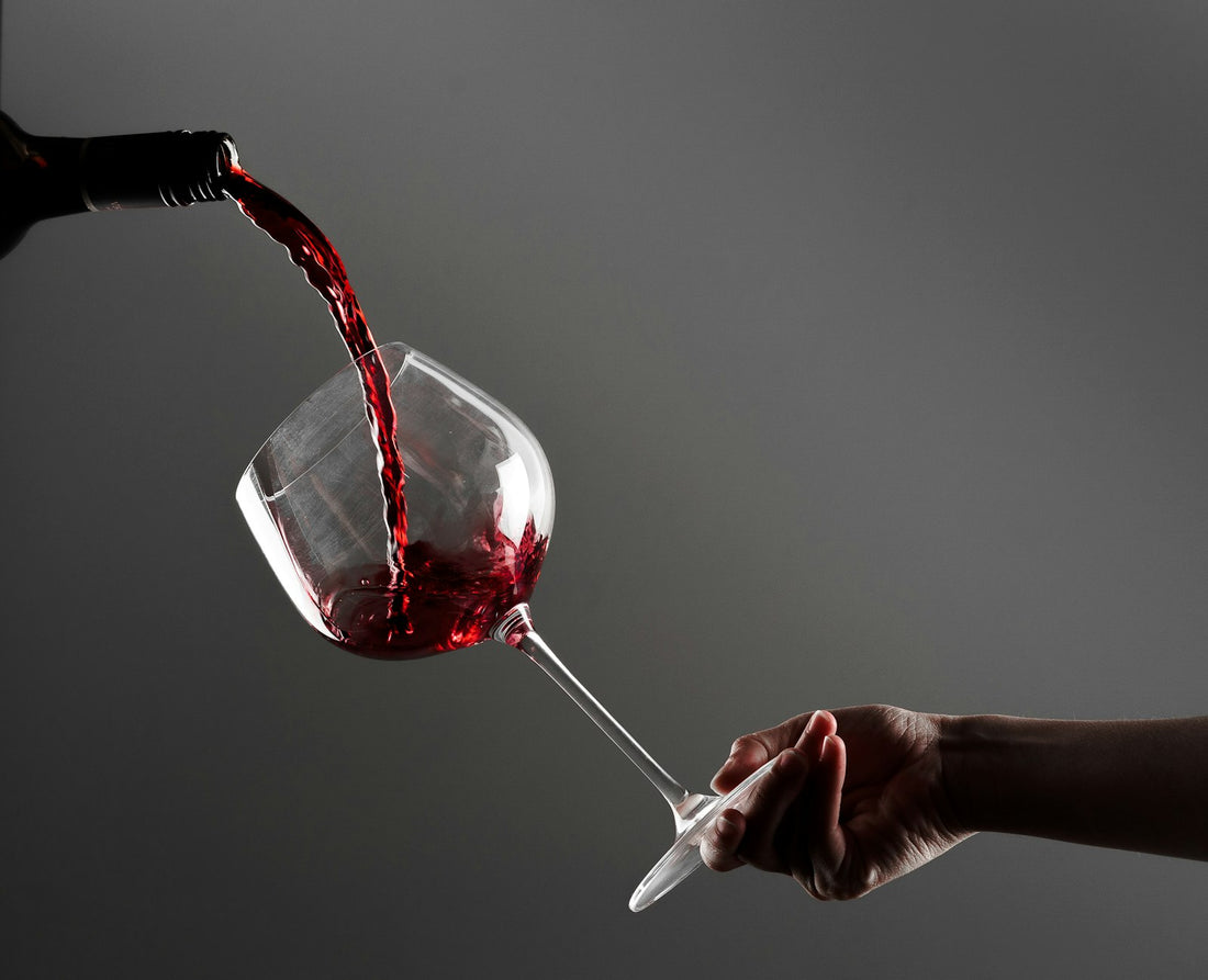 A glass of red wine being poured against a neutral background