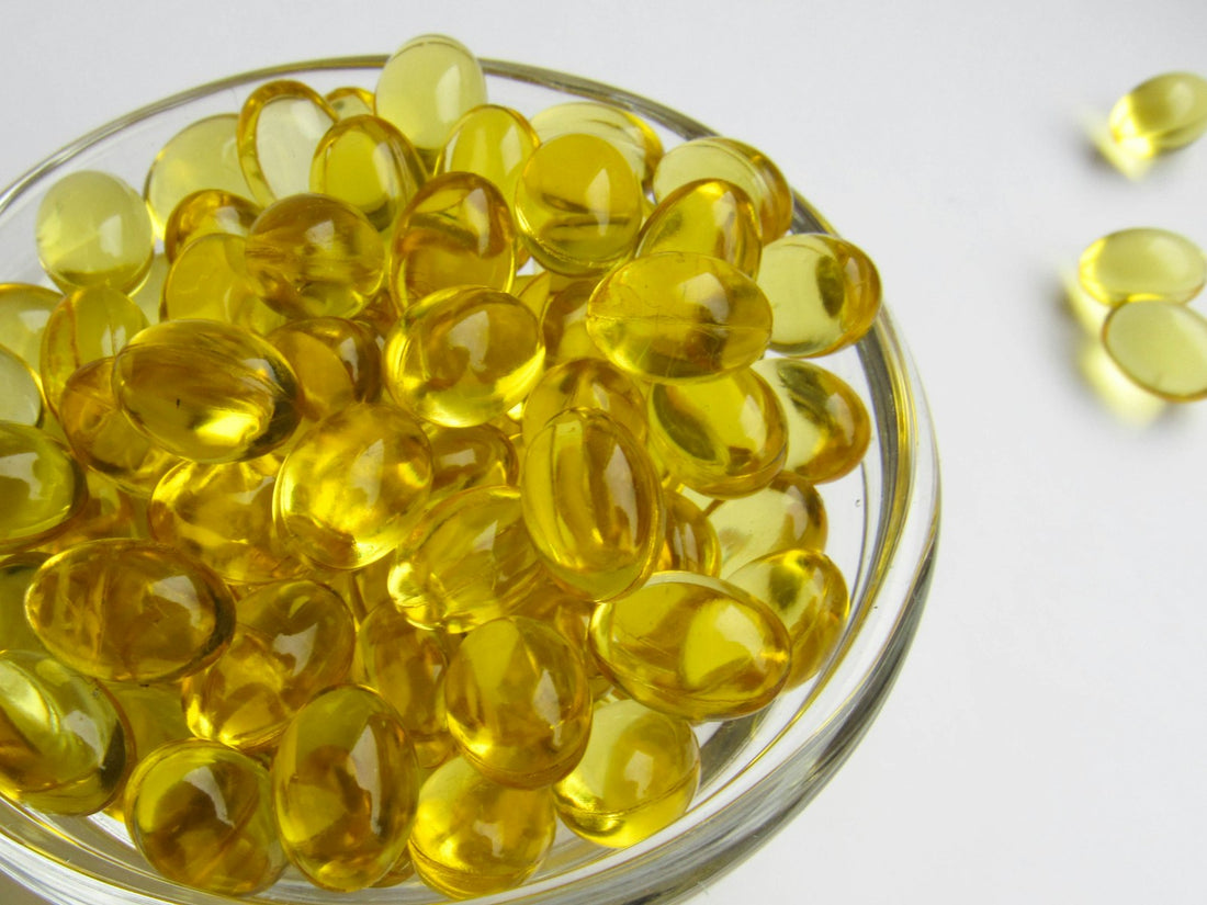A glass bowl of yellow vitamin D softgel capsules on a white surface