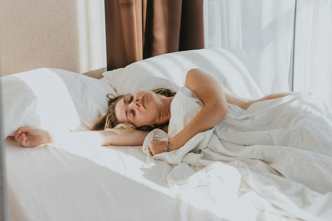 A woman sleeping peacefully on her side in a bright white bed