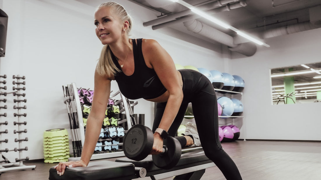 Woman doing a single arm dumbbell row on a bench in a bright gym