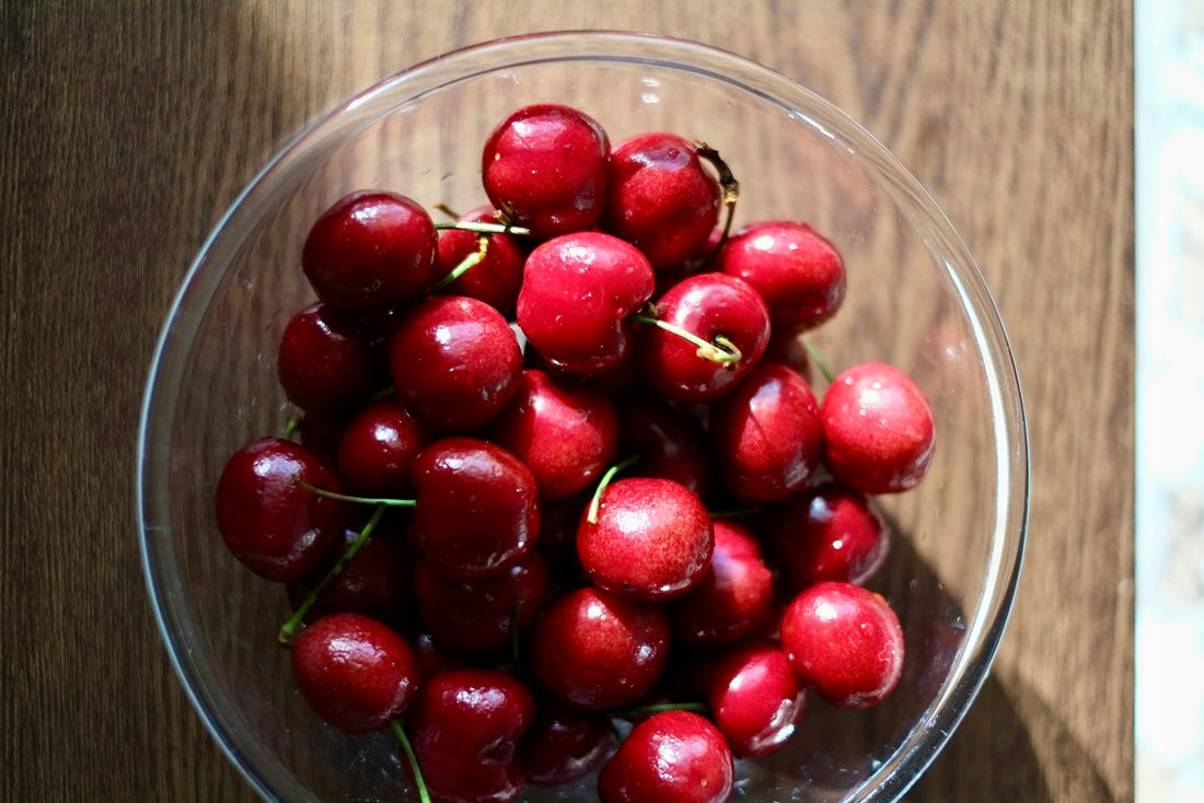A clear glass bowl full of fresh red cherries on a wooden table