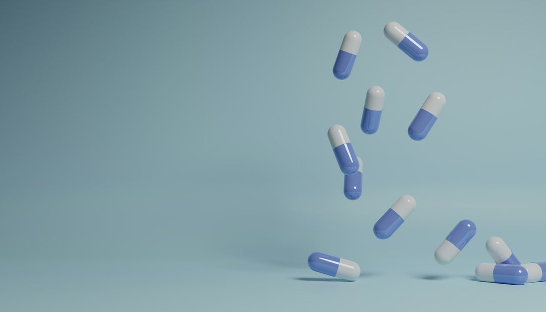 Blue and white vitamin capsules falling against a soft teal background