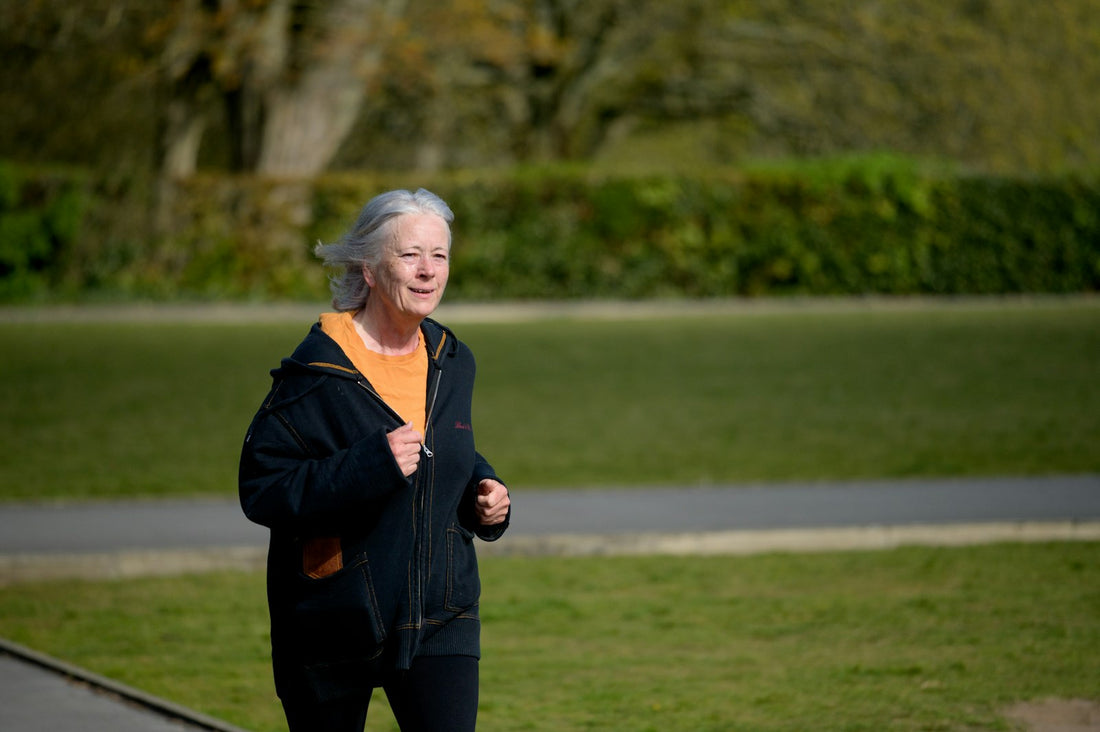 An older woman walking briskly along a path in a green park