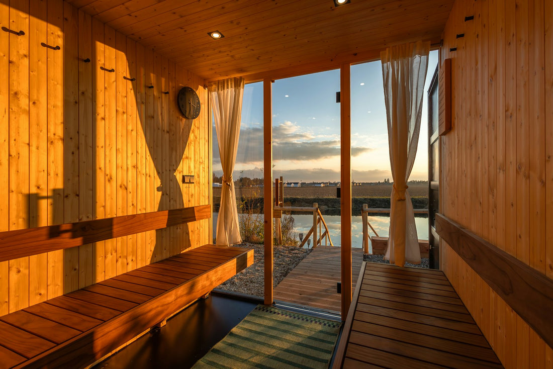 A wooden sauna interior with a bench and an open door looking out to a lake at sunset.