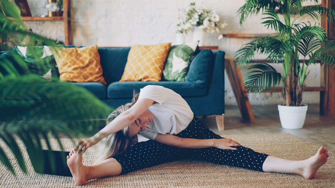 Woman doing a seated side stretch on the floor of a bright living room