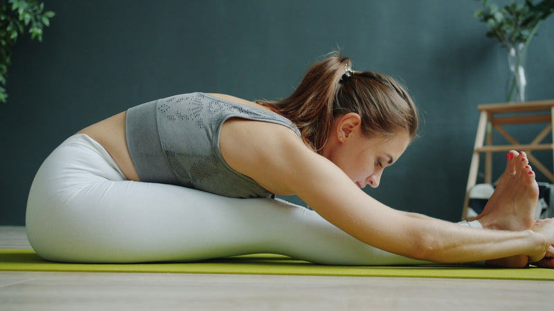 A woman doing a seated forward stretch on an exercise mat