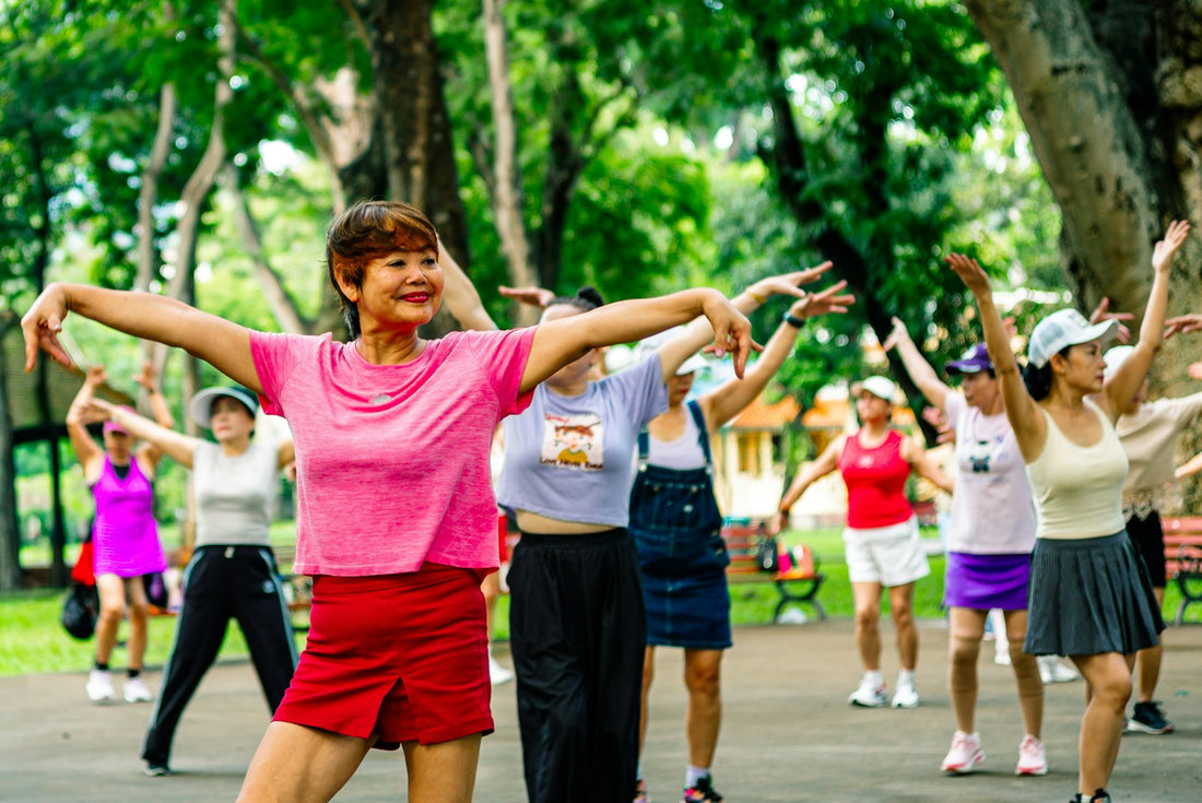 A group of people exercising together outdoors in a park, arms raised mid-movement