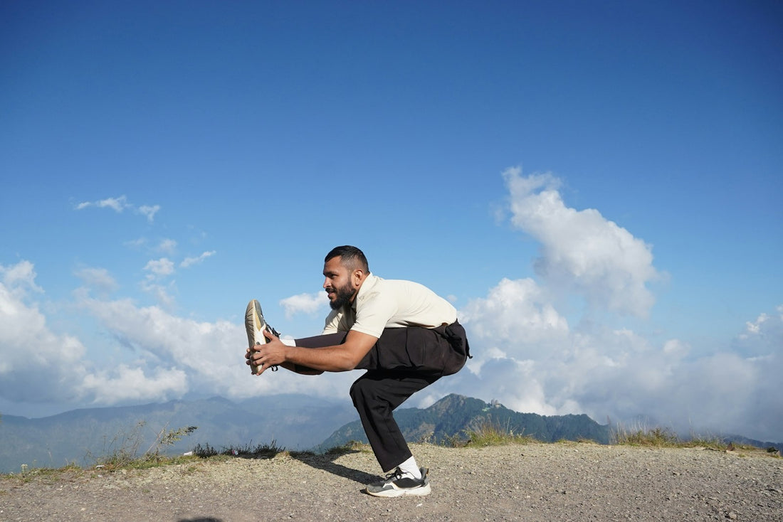 A person doing a standing stretch outdoors on a hilltop under a bright sky