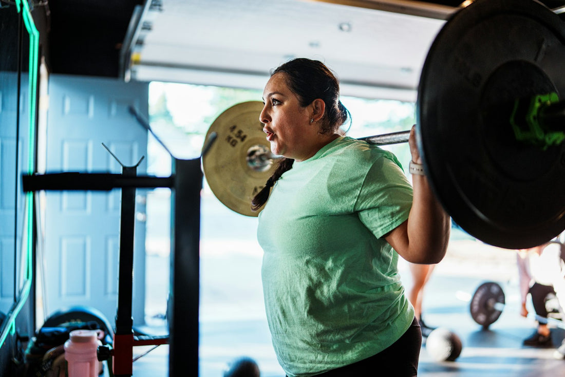 A person doing a barbell back squat in a bright gym.