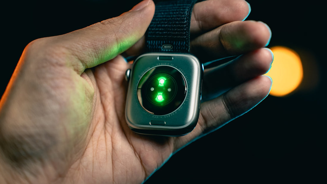 A hand holding a smartwatch with its green heart-rate sensor glowing on the back