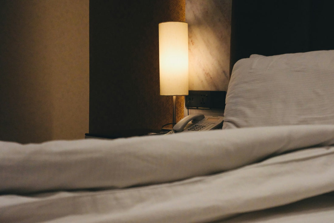 Dim bedside lamp over a rumpled duvet at night