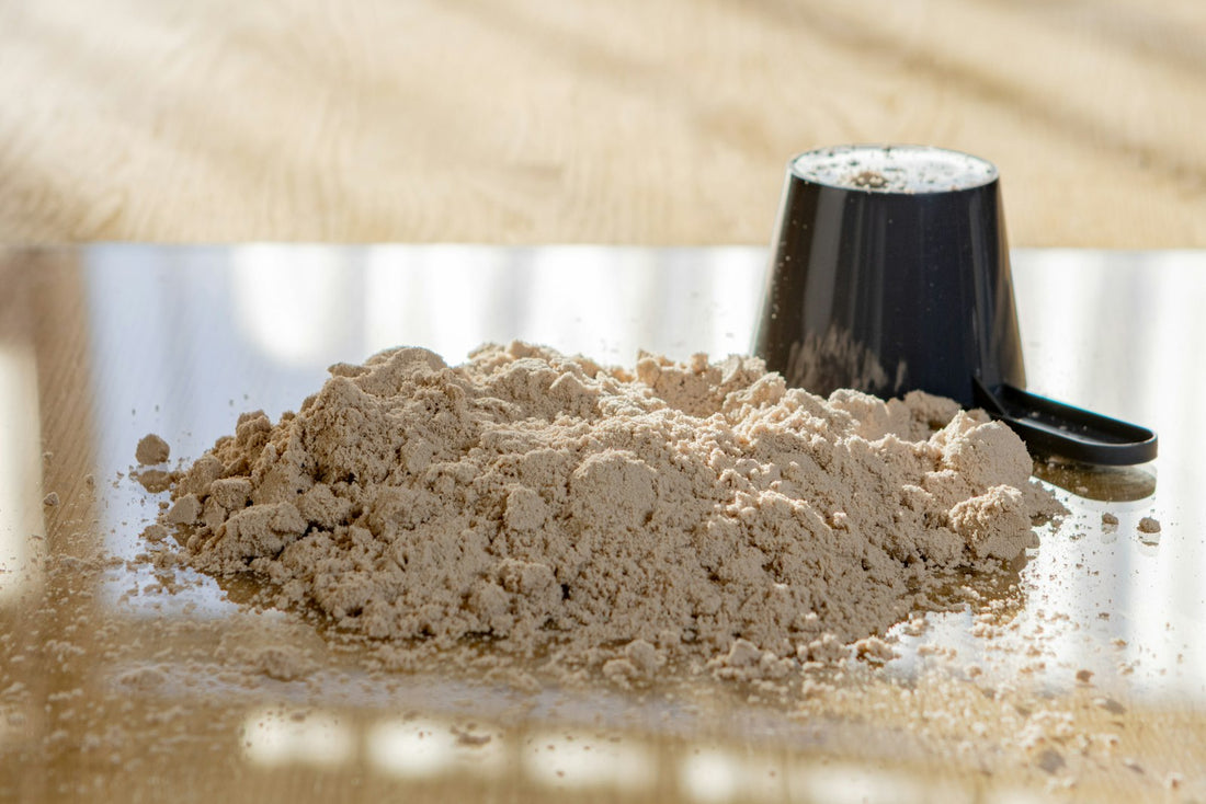 A pile of protein powder with a black scoop on a light surface