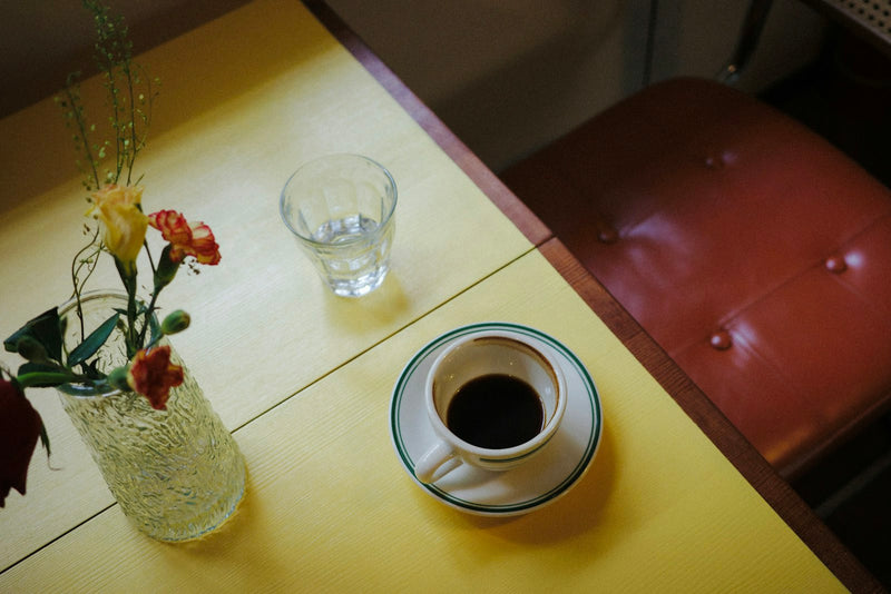 A cup of black coffee and a glass of water on a warm cafe table