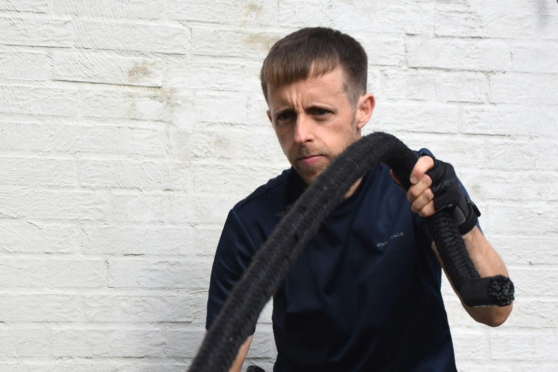 A man training hard with a heavy battle rope against a white brick wall