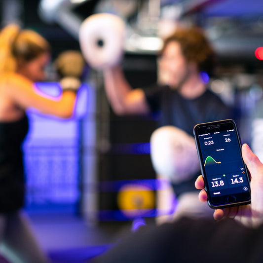 Coach reviewing training stats on a phone while a client trains