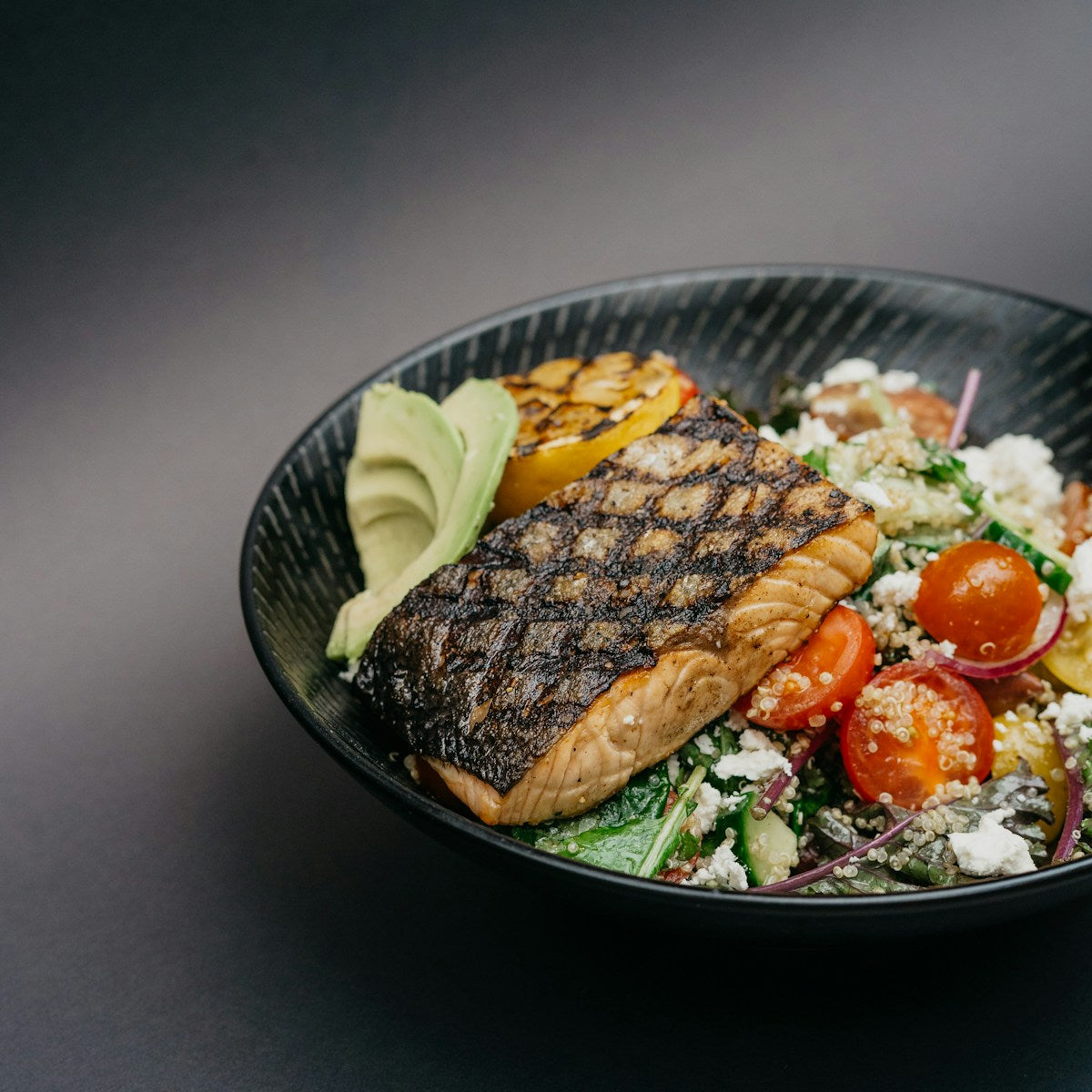 Grilled salmon bowl with avocado and quinoa on a black plate