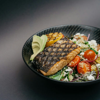 Grilled salmon bowl with avocado and quinoa on a black plate